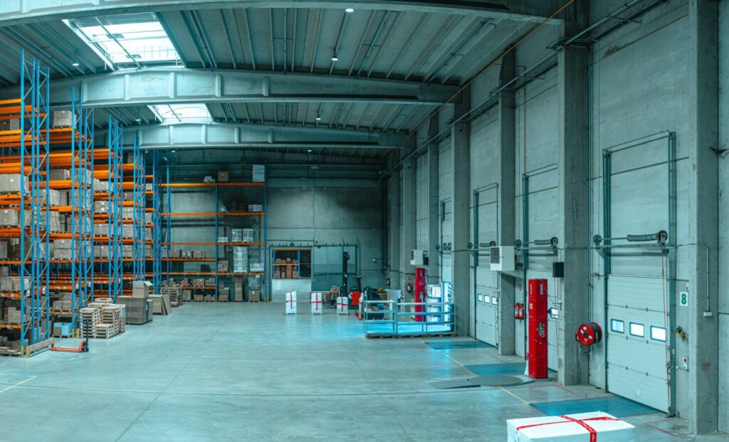Interior of large warehouse; fire extinguishers and other fire safety tools on wall near door.