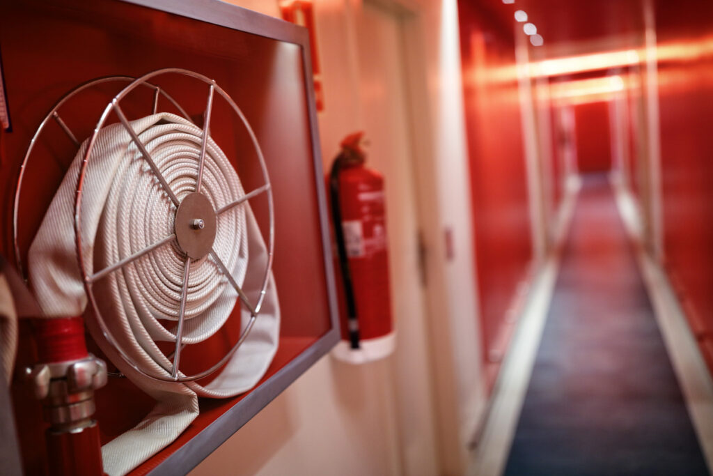 Close view of a fire hose and fire extinguisher on a wall in an apartment complex hallway.