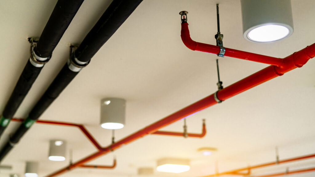 Red pipes for fire sprinkler system installed on a ceiling in a commercial building.