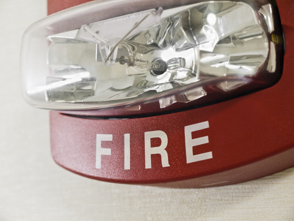 Red fire alarm with strobe light on wall in school.