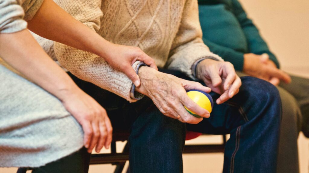 Close-up of nurse's hand holding the wrist of an older patient, who is holding a soft colorful ball.